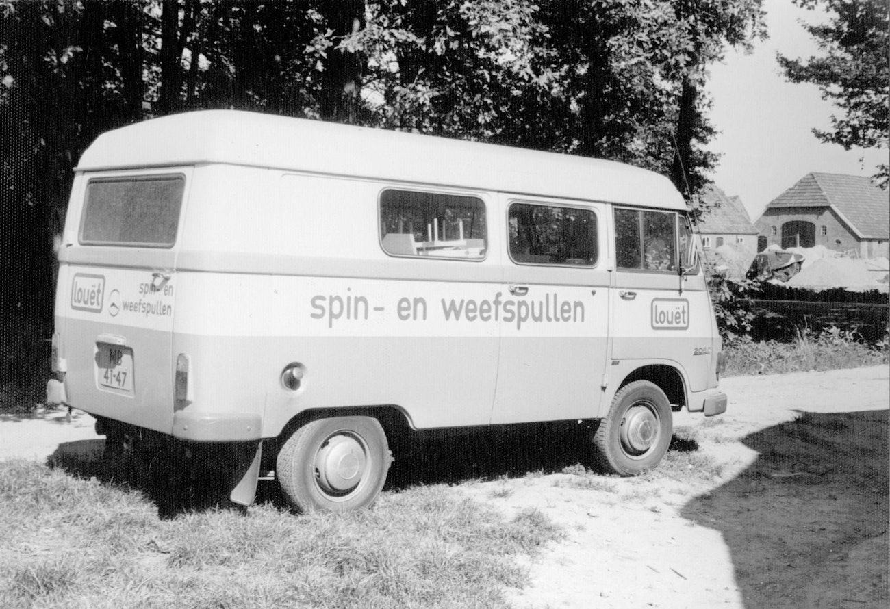 Black-and-white photo of small bus that says, “spin- en weefspullen”